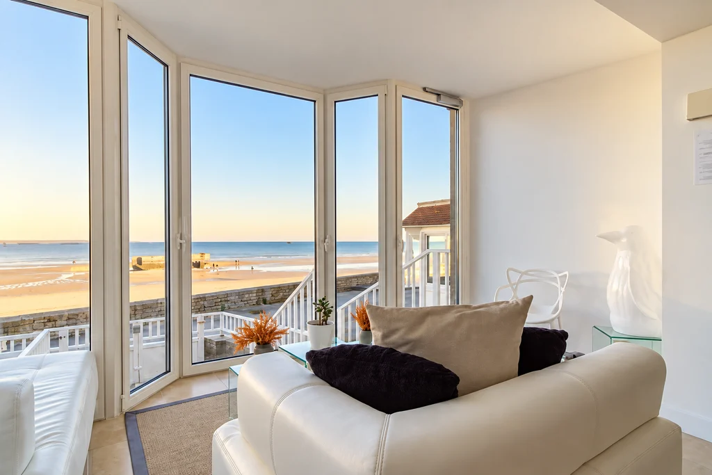 Salon blanc avec canapé et baies vitrées ouvertes sur la mer