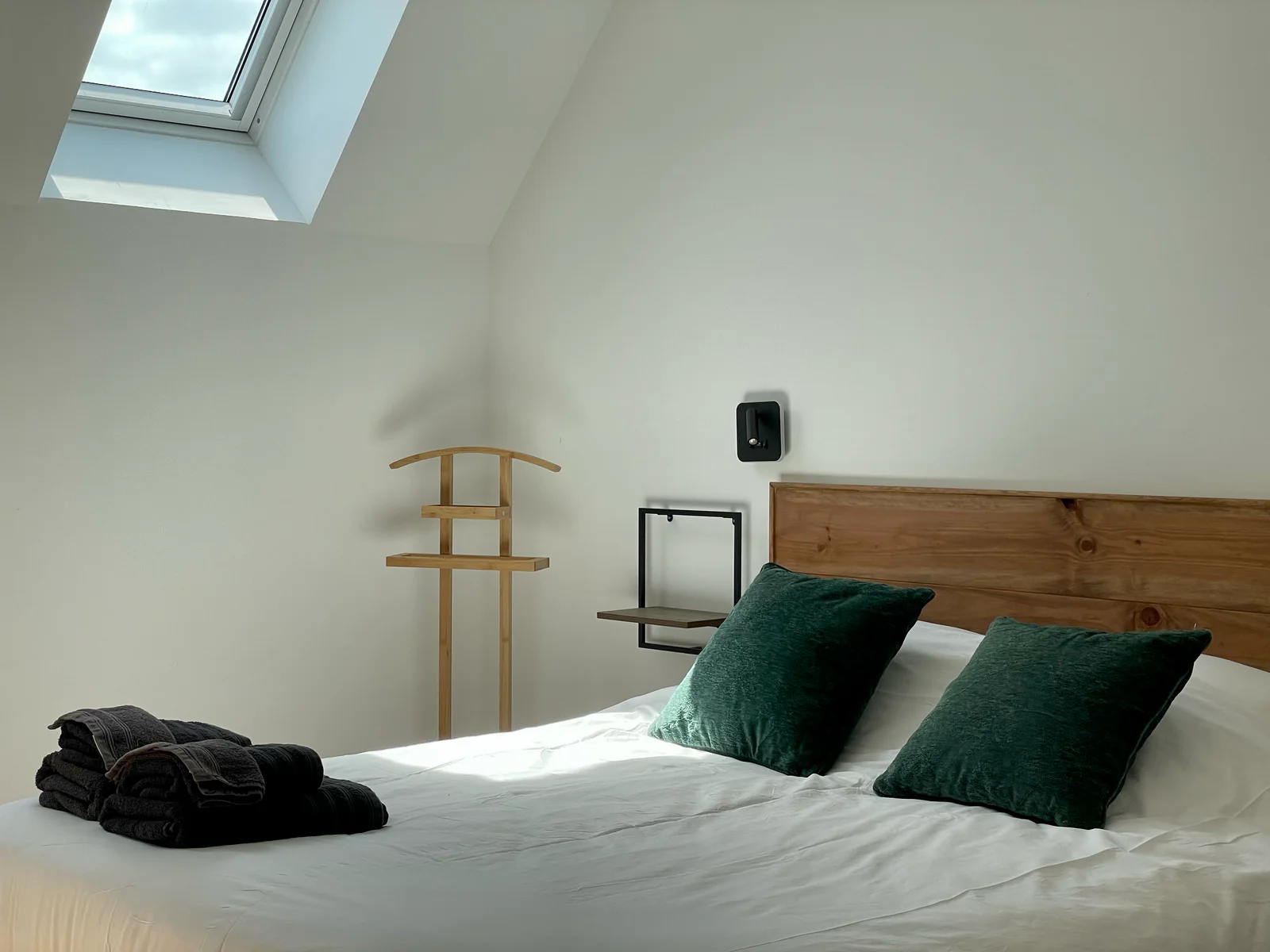 Chambre du Logis de Courtelay avec lit blanc, coussins verts et serviettes pliées sous le velux