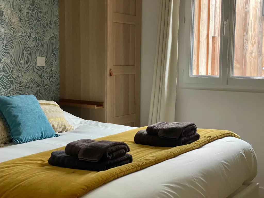 Serviettes pliées sur le lit préparé de La Comète, avec linge blanc et plaid jaune