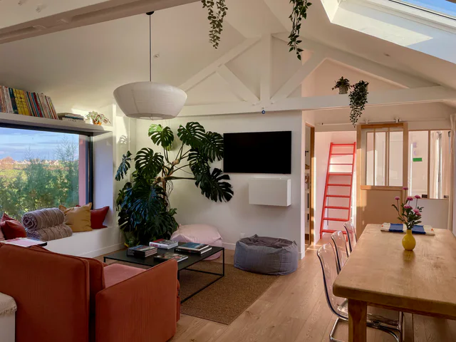 Salon et salle à manger de La Maison Rose Ciel, avec canapé rose, plantes et échelle vers la mezzanine